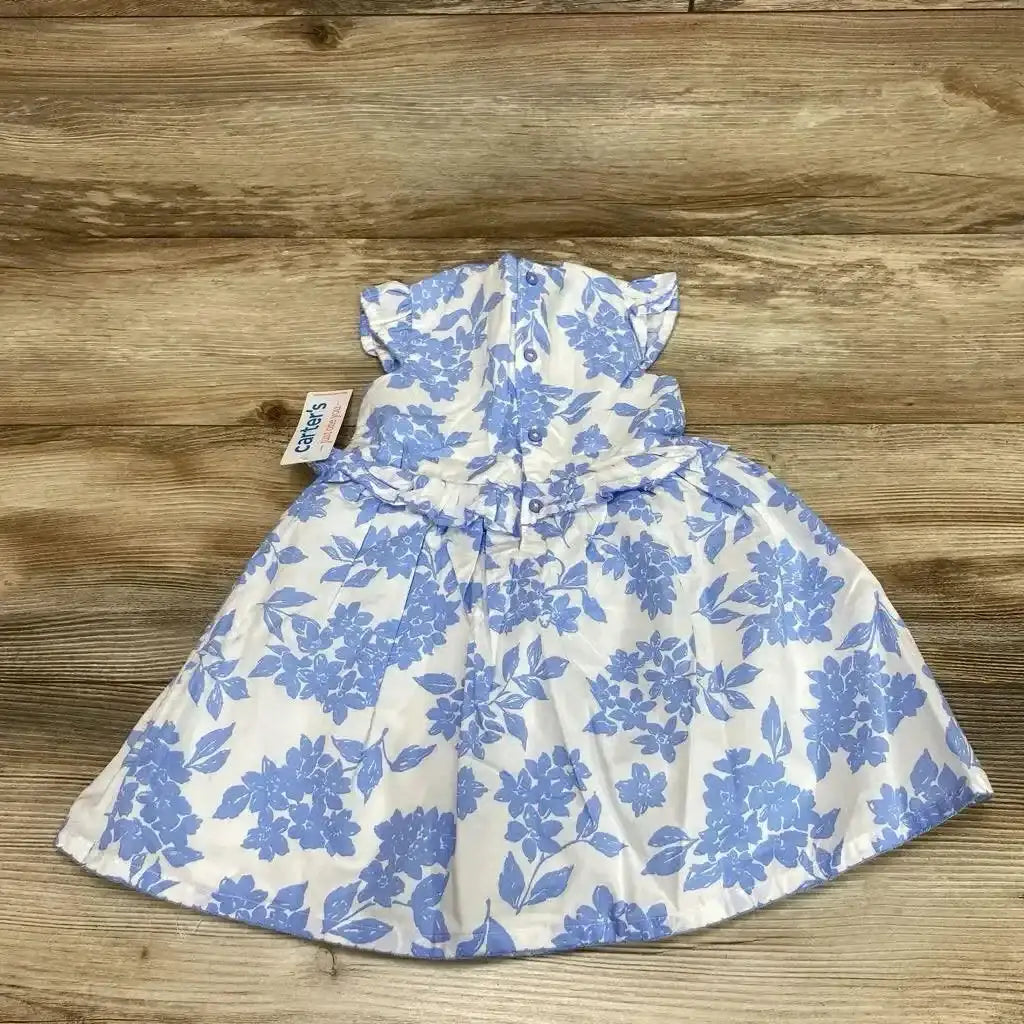 Flat lay of white baby dress and matching bloomers with blue floral print showing back button closure on wood background