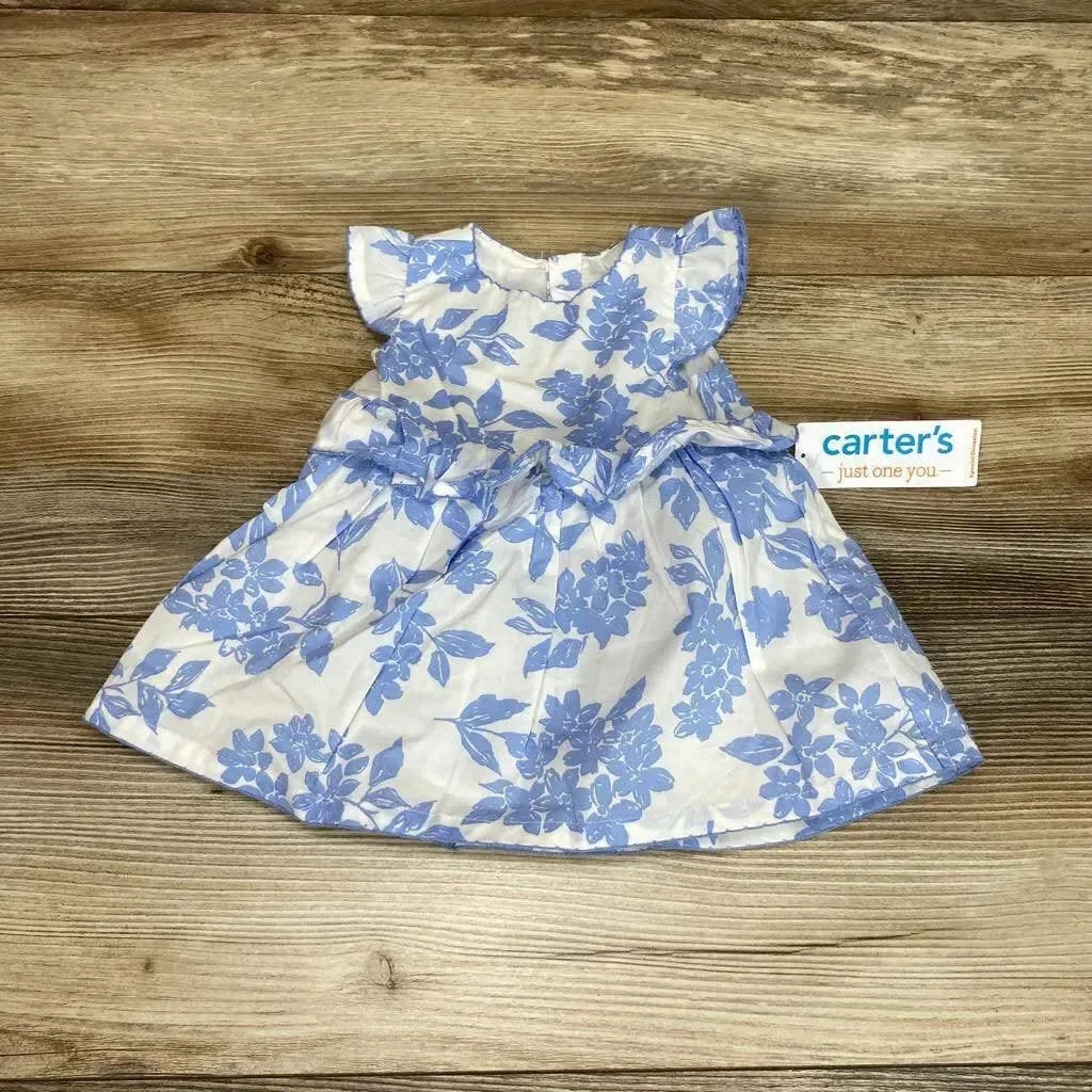 Flat lay of newborn white dress with blue floral print showcasing flutter sleeves and gathered skirt on wooden floor background