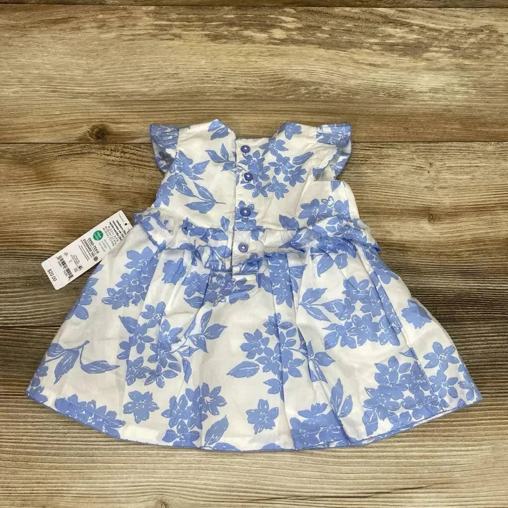 Top down flat lay of baby white dress with blue floral print showing button back and ruffle cap sleeves on wooden background