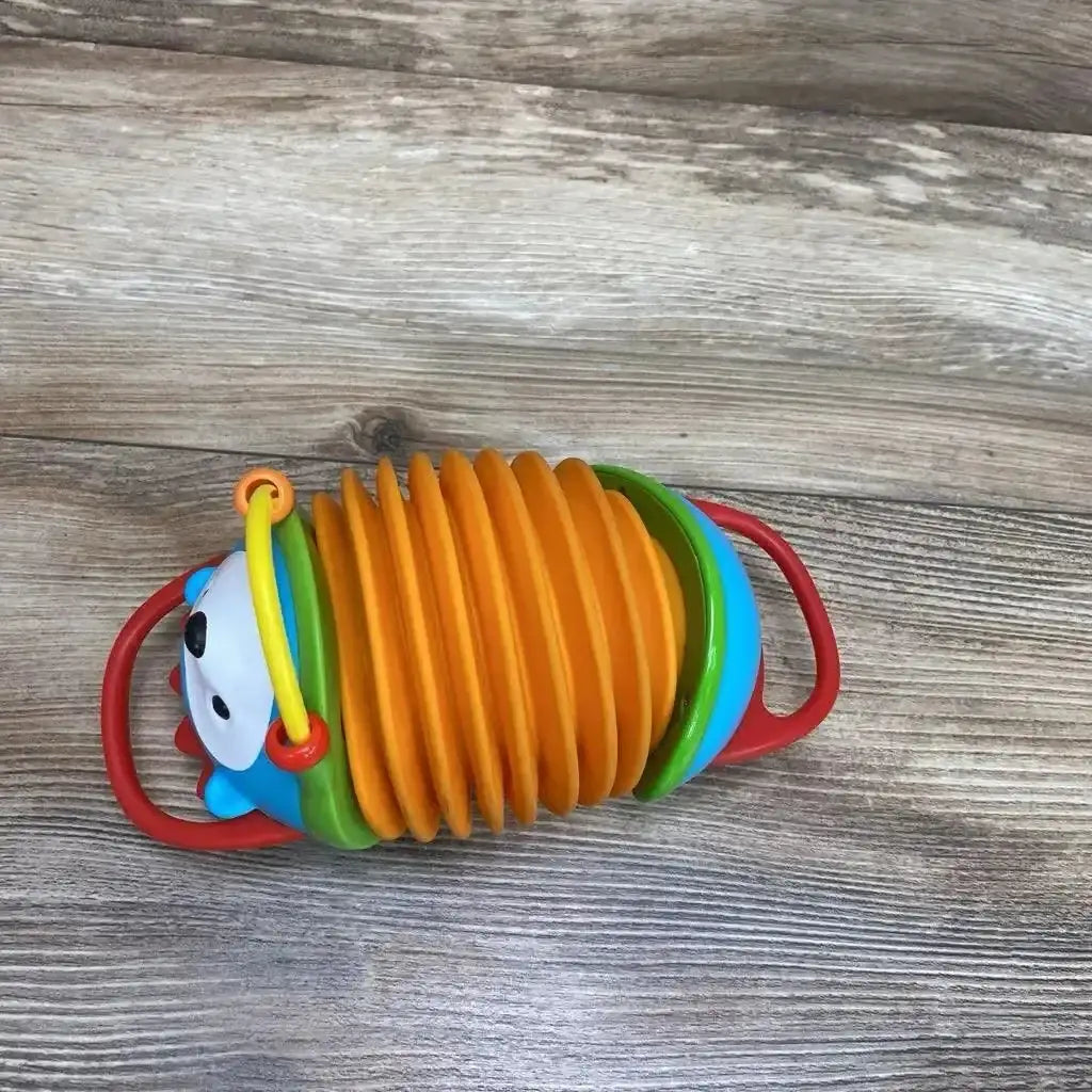 Top-down view of Skip Hop hedgehog accordion toy showing orange bellows, red handles, and blue hedgehog head on wood floor