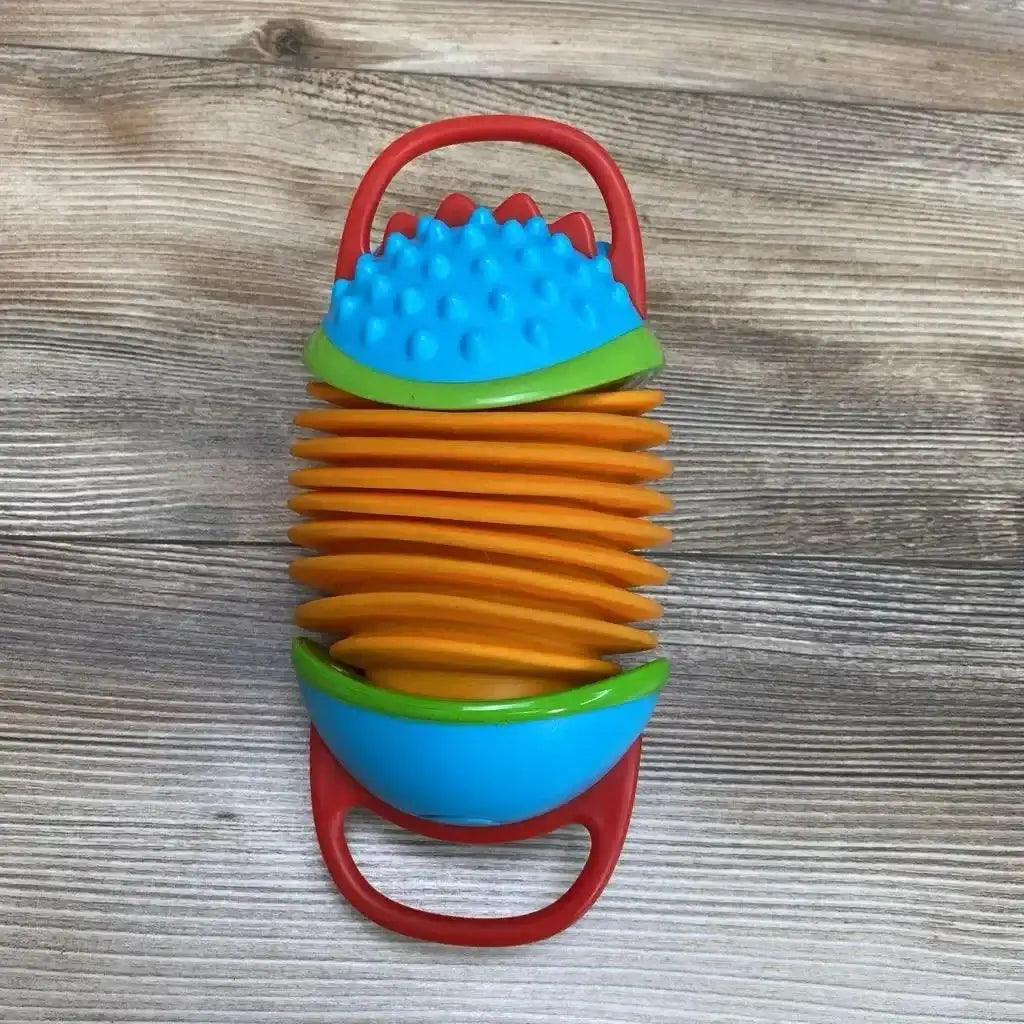Top-down view of Skip Hop hedgehog accordion toy with orange bellows, blue textured ends and red handles on wood background