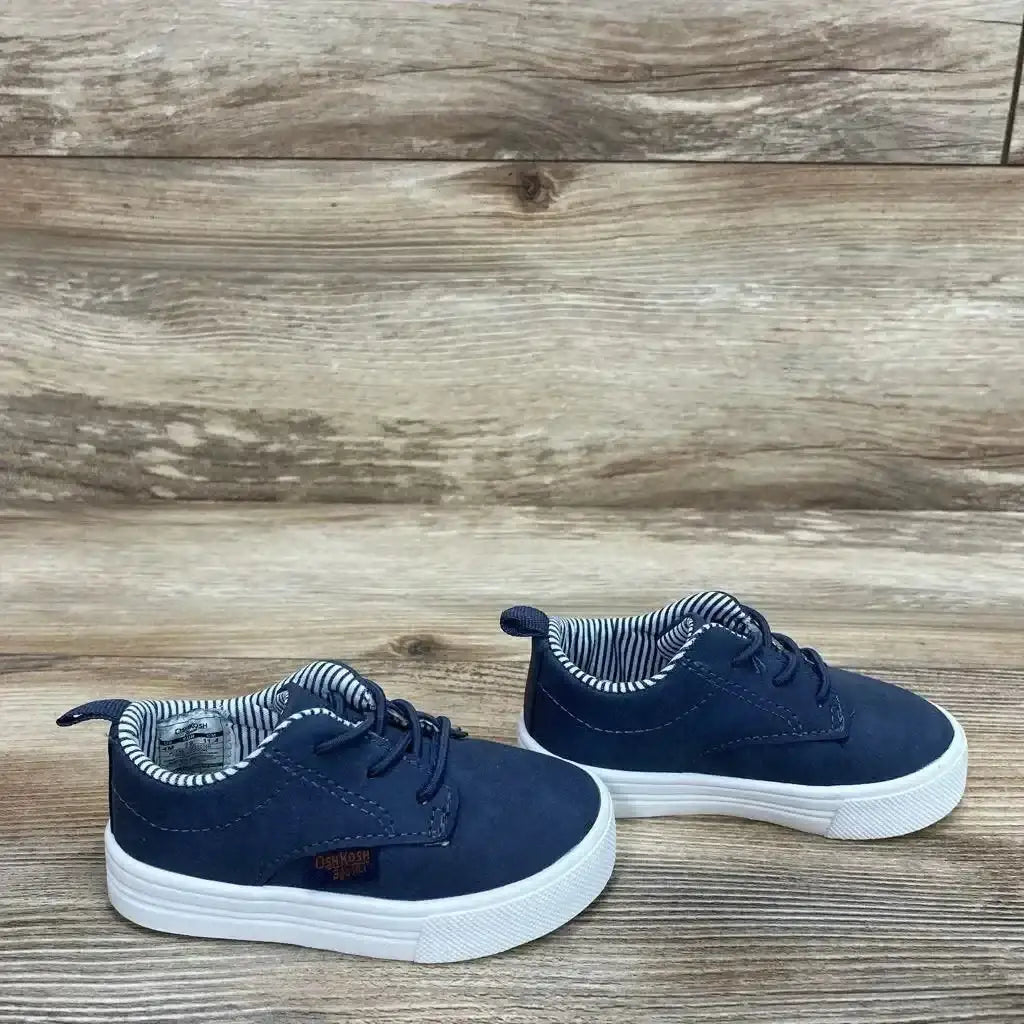 Angled view of OshKosh Putney Oxford Casual Sneakers Sz 4c showcasing faux laces, white soles, and striped lining on wood