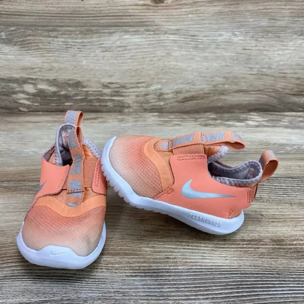 Side view of Nike Flex Runner Sneakers in coral pink with silver Nike swoosh pull tabs and white sole on wood plank floor