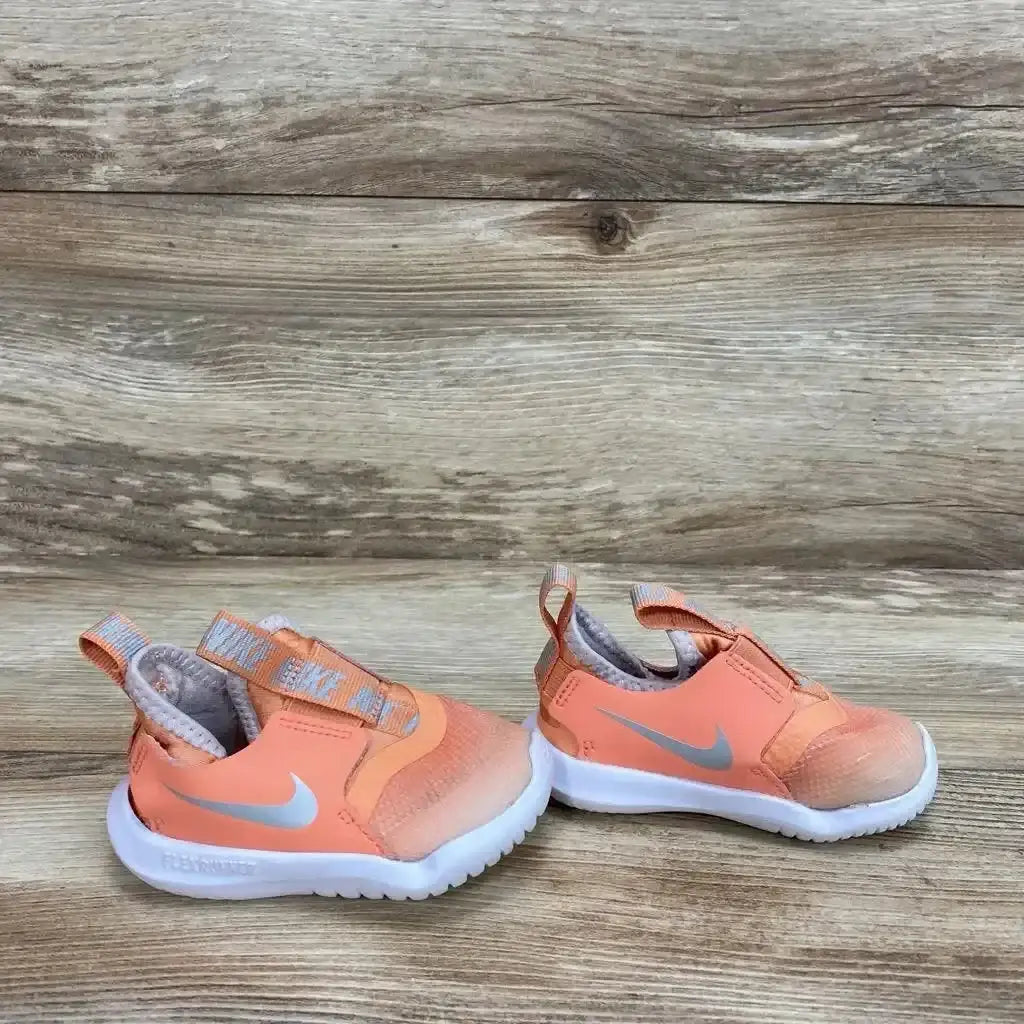 Side view of orange Nike Flex Runner sneaker showing slip-on elastic strap, gray Swoosh and white sole on wood background