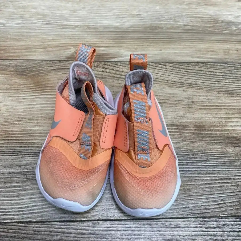 Top view of Nike Flex Runner toddler sneakers in coral peach with grey swoosh and slip-on strap on wood plank floor