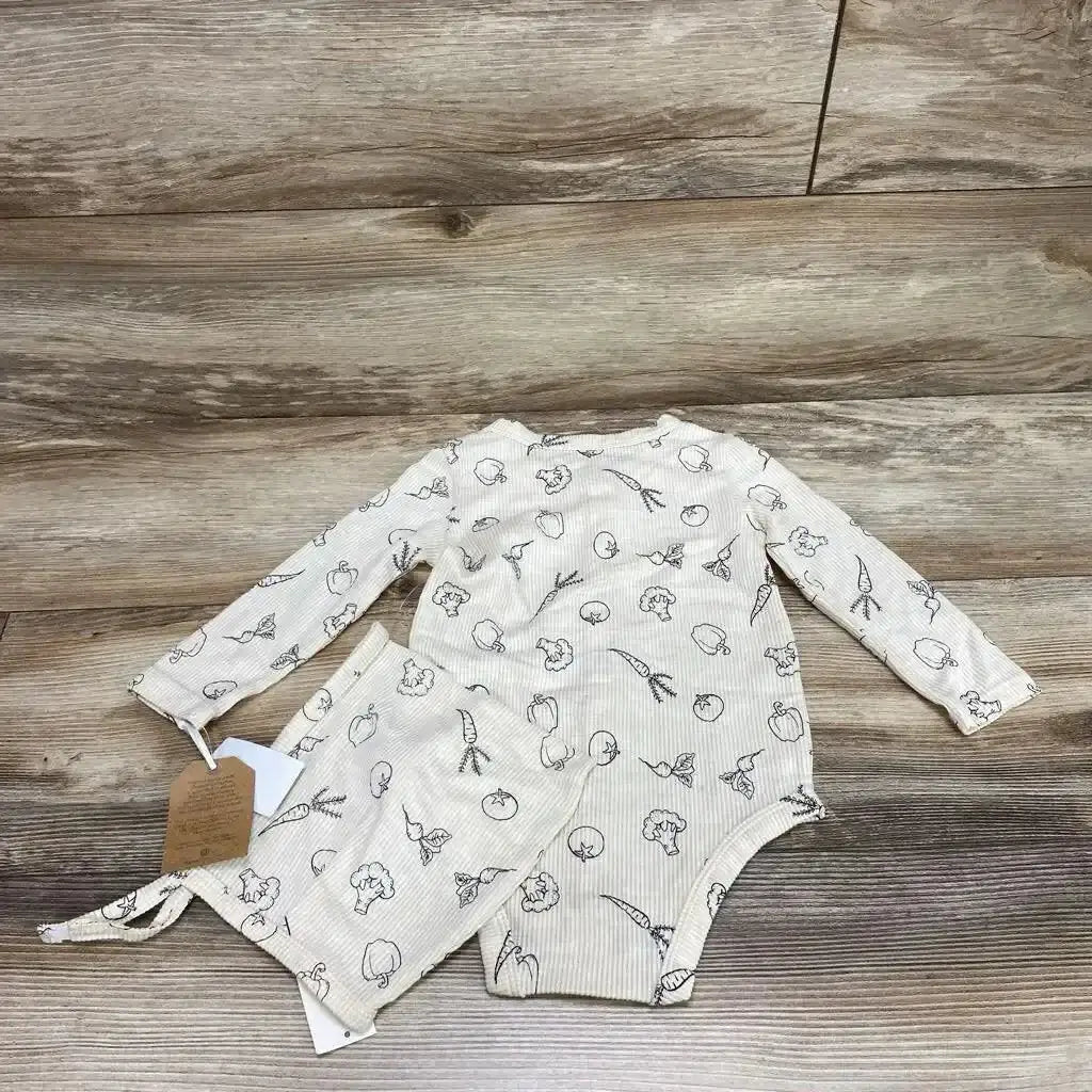 Flat lay of cream ribbed long-sleeve baby bodysuit and matching bonnet with vegetable line-drawing print on wood background