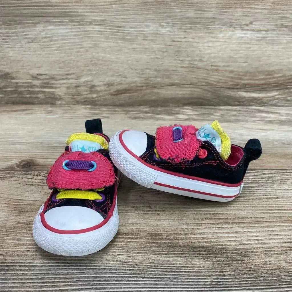 Front view of toddler black Converse low-top sneakers with pink double tongues and yellow accents on wood