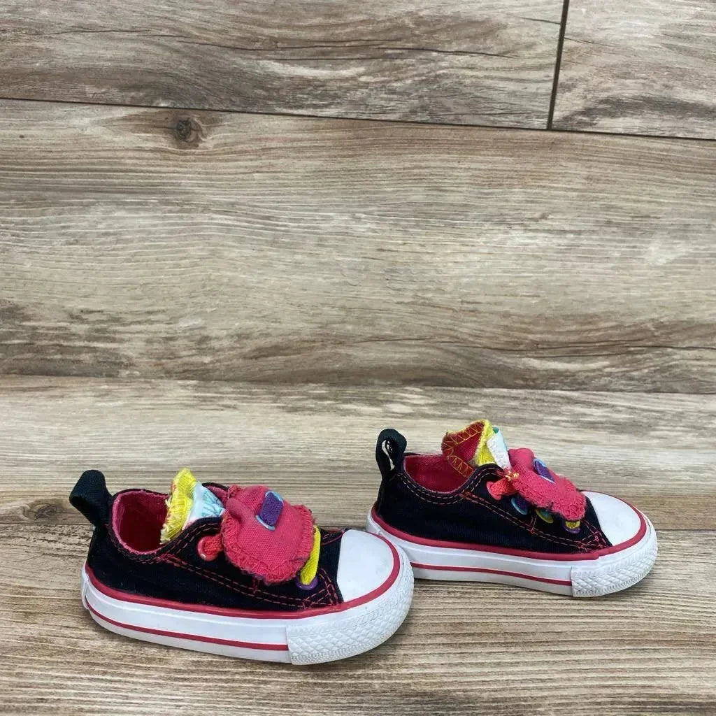 Side view of toddler black Converse Chuck Taylor double-tongue low-top sneakers with pink and yellow tongues on wood background