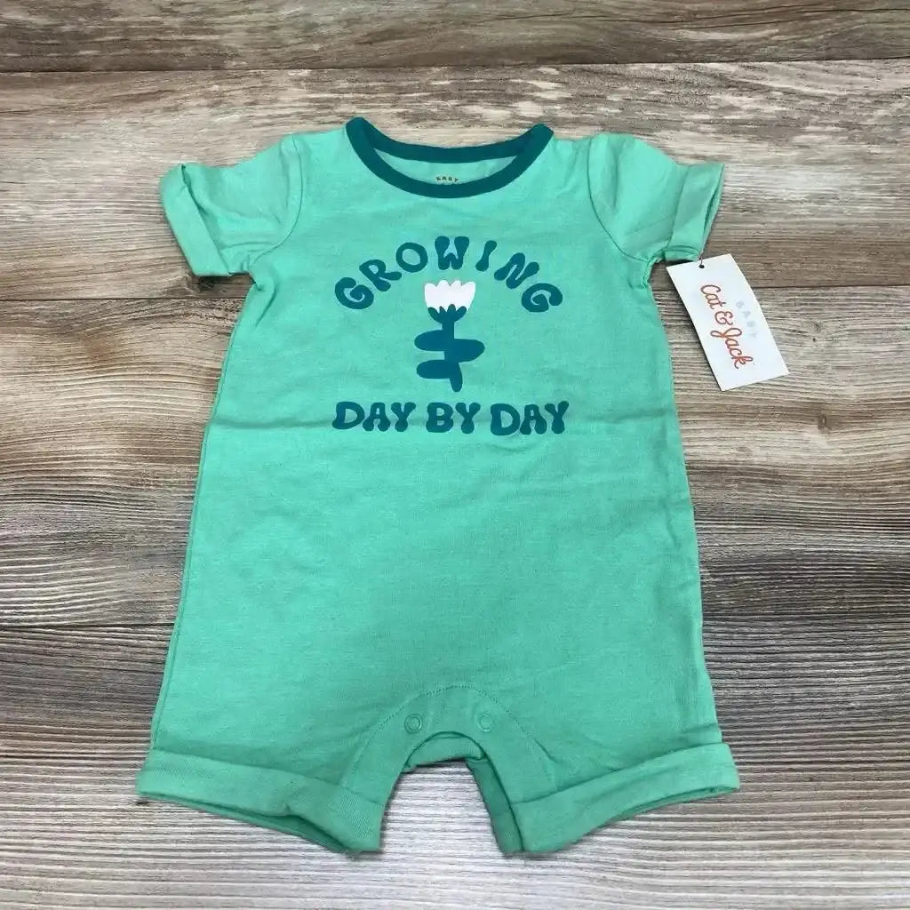 Flat lay of green Cat and Jack romper (3-6m) showing GROWING DAY BY DAY flower print and crotch snaps on wood background