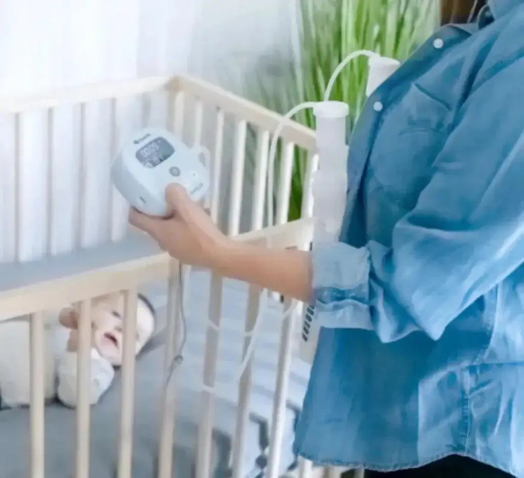 Side view of Mya hospital-strength double electric breast pump held by a person, showing digital display and tubing beside a baby in a crib