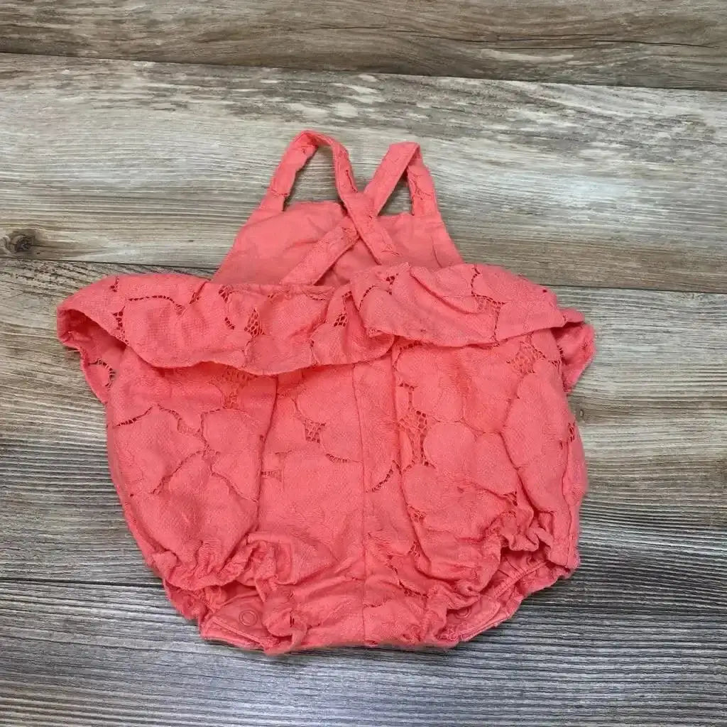 Top-down view of coral-pink lace baby peplum romper (3–6M) with ruffle, crisscross straps and snap crotch on wood background