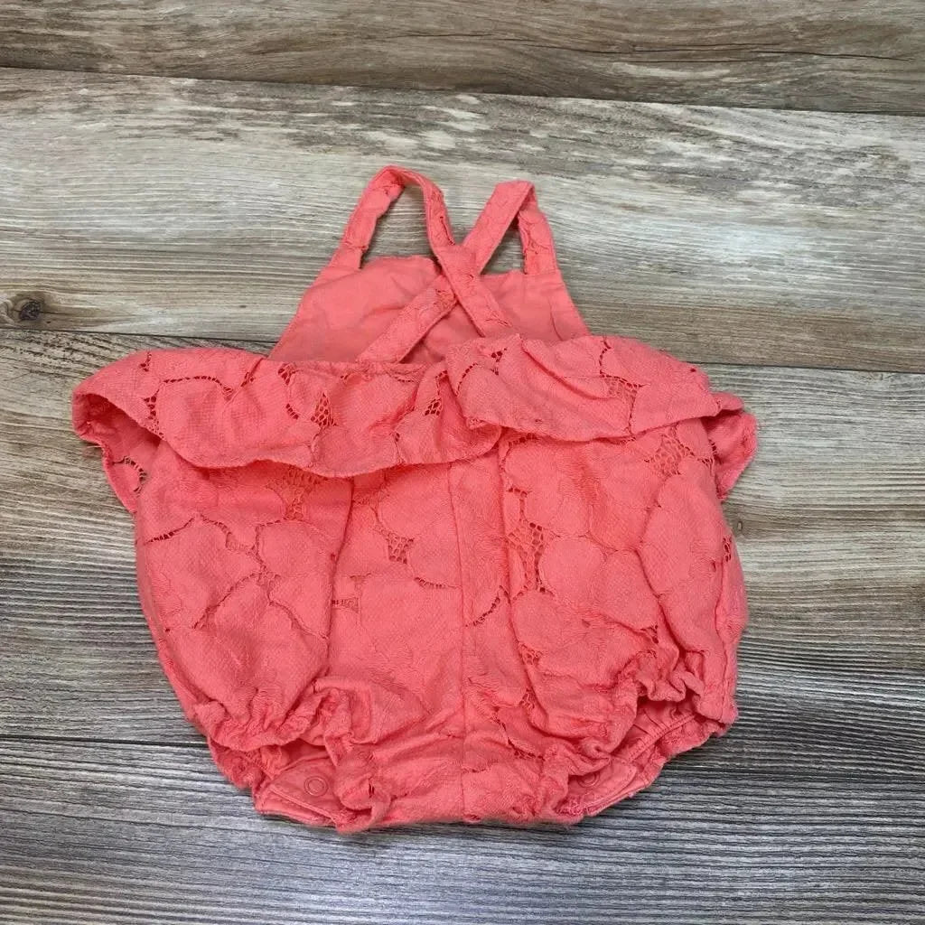 Top-down view of coral-pink lace baby peplum romper (3–6M) with ruffle, crisscross straps and snap crotch on wood background
