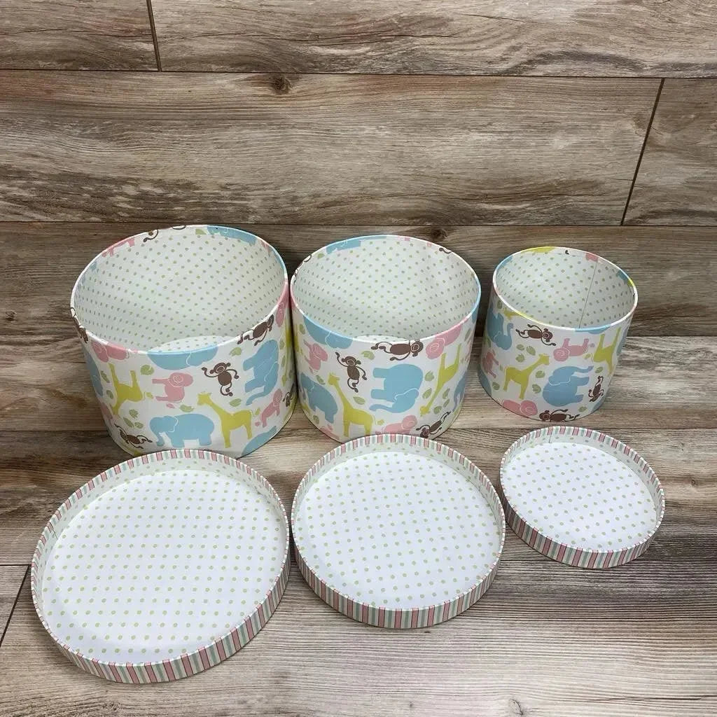 Front view of three round nesting storage trunks with pastel animal print, lids removed and placed in front on wood floor