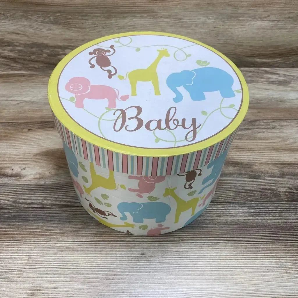 Top-front view of round nesting storage trunk showcasing pastel animal pattern and 'Baby' text on lid with woodgrain tabletop background
