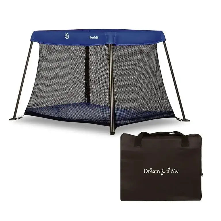 Angled view of Dream On Me travel playard, blue top, mesh sides and angled legs, with black carrying bag on white background