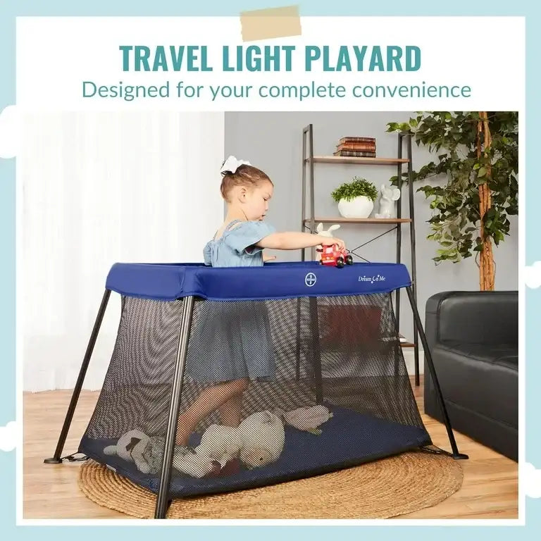 Three-quarter view of Dream On Me Travel Light playard in blue showcasing mesh sides and slim black frame with child playing on rug in living room