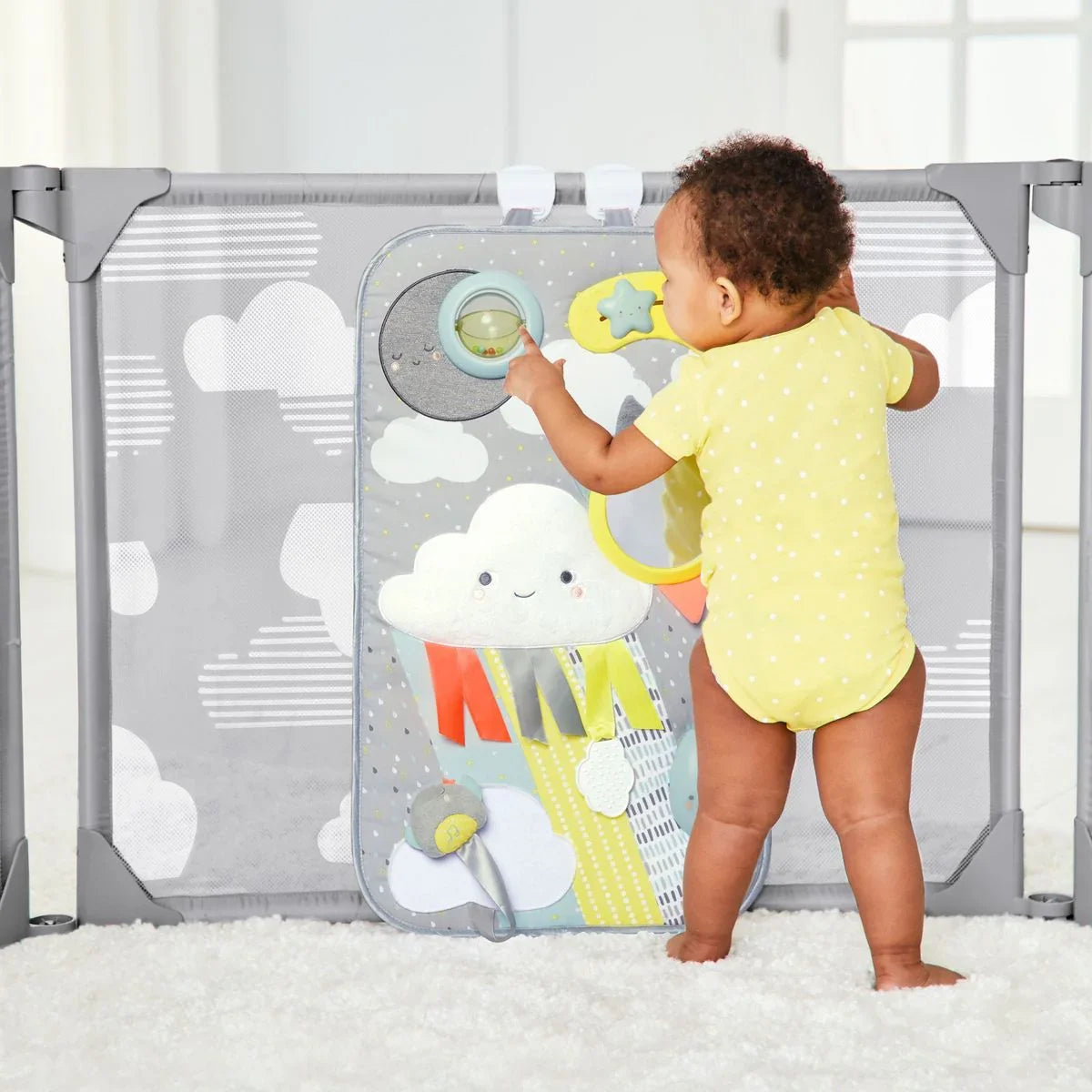 Baby in yellow onesie plays at cloud-themed activity center in gray playpen