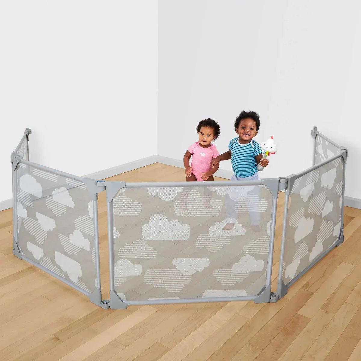 Two toddlers inside a cloud-patterned baby playpen on a wooden floor