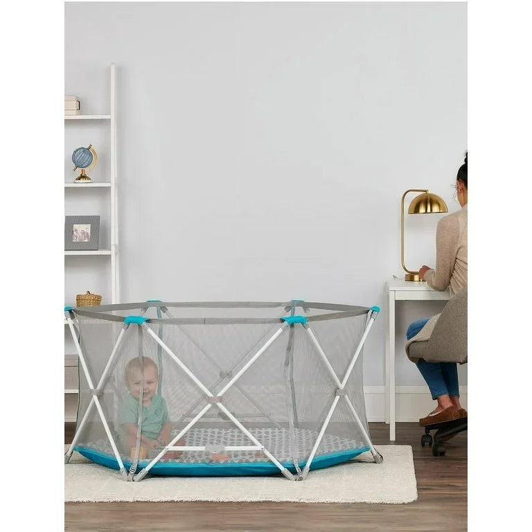 Baby in portable playpen with mesh sides near woman working at desk at home