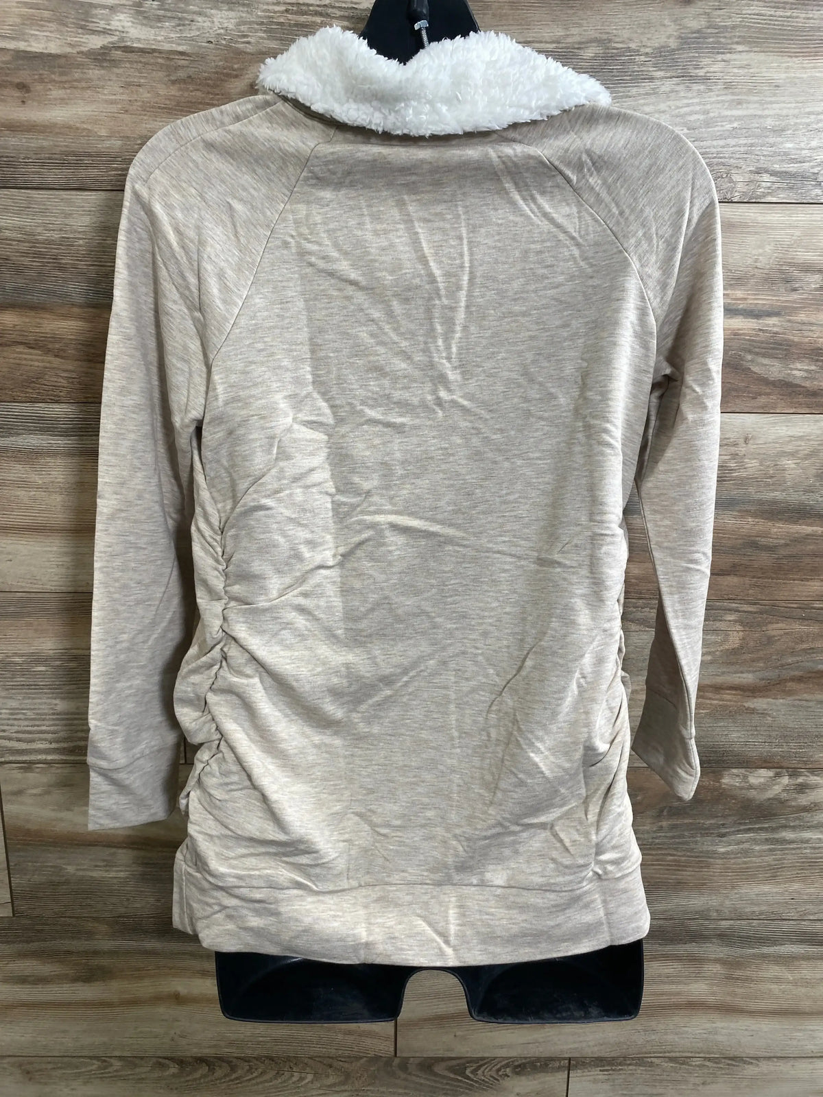 Back view of oatmeal maternity sweatshirt showing white sherpa collar and side ruching on a hanger against wood background
