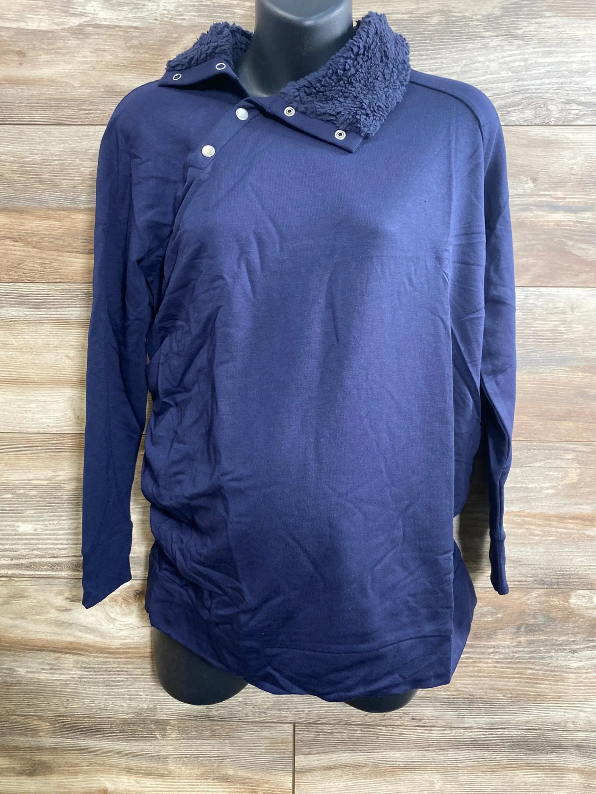 Front view of NEW Isabel Maternity navy sweatshirt on mannequin showcasing sherpa collar snap placket and ruched sides on wood plank floor