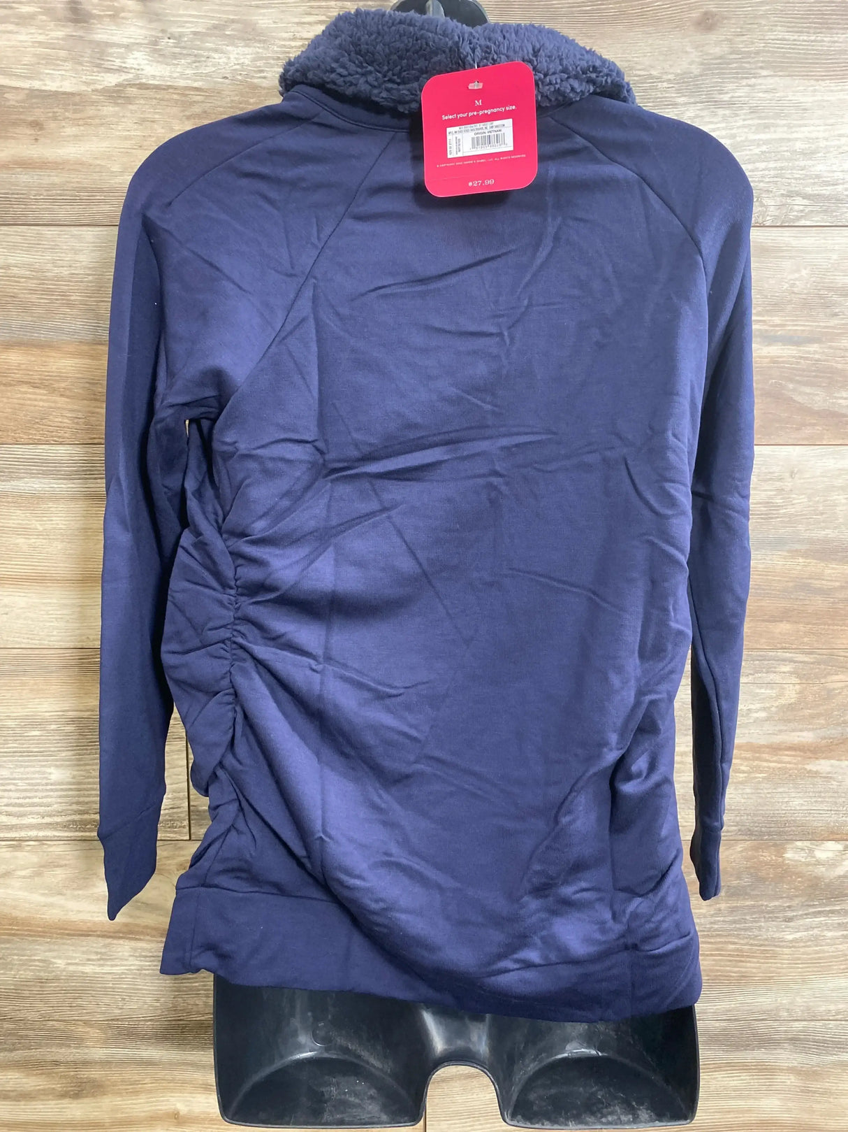 Back view of navy Isabel maternity sweatshirt showcasing sherpa collar and side ruching for pregnancy fit on wood background