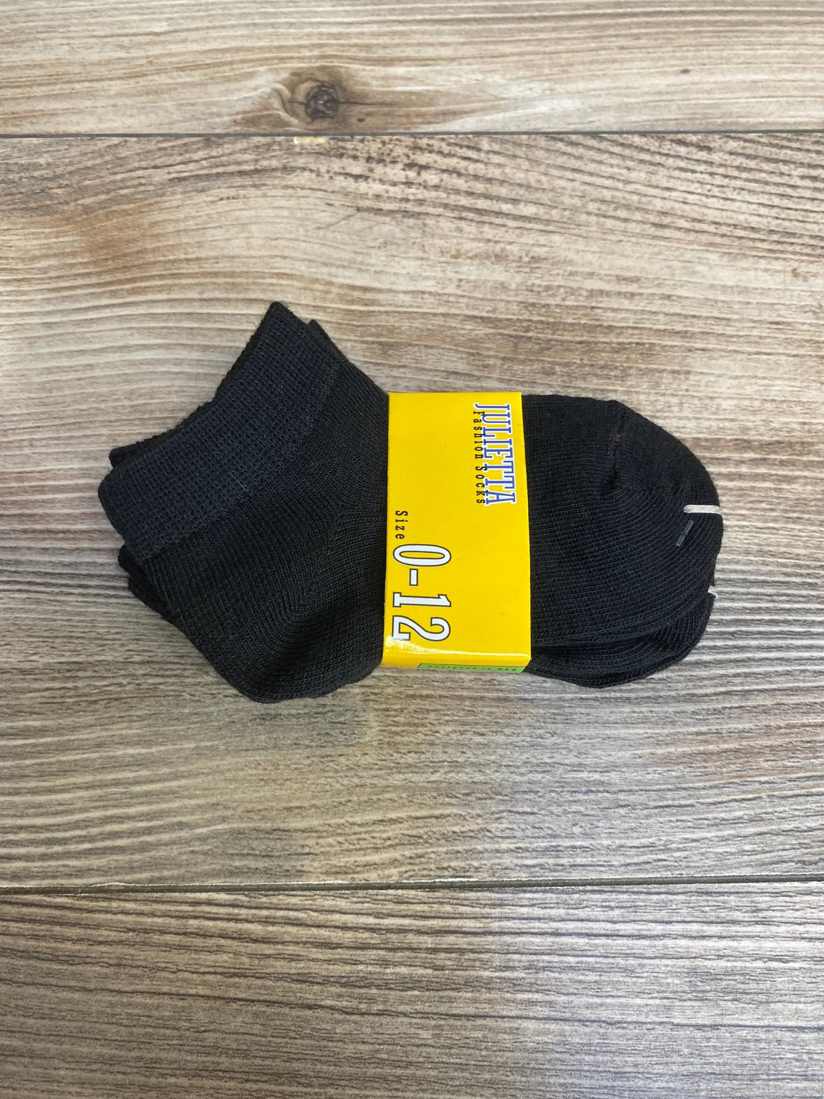 Top-down view of 3-pack black baby ankle socks showing yellow Julietta label reading Size 0-12 on wood background