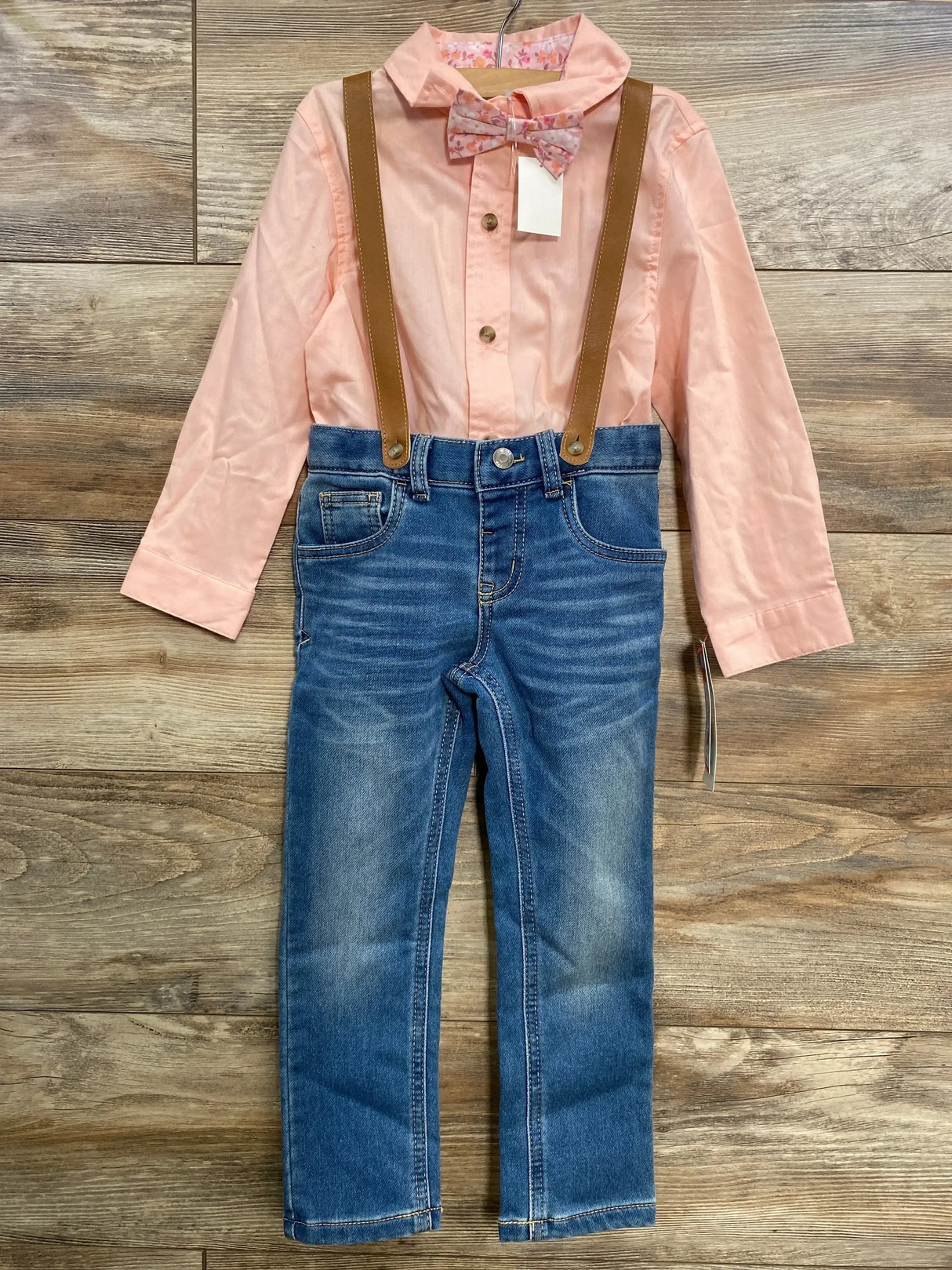 Front of Cat and Jack suspender set showing pink shirt with floral bow tie, brown suspenders and blue jeans on wood floor