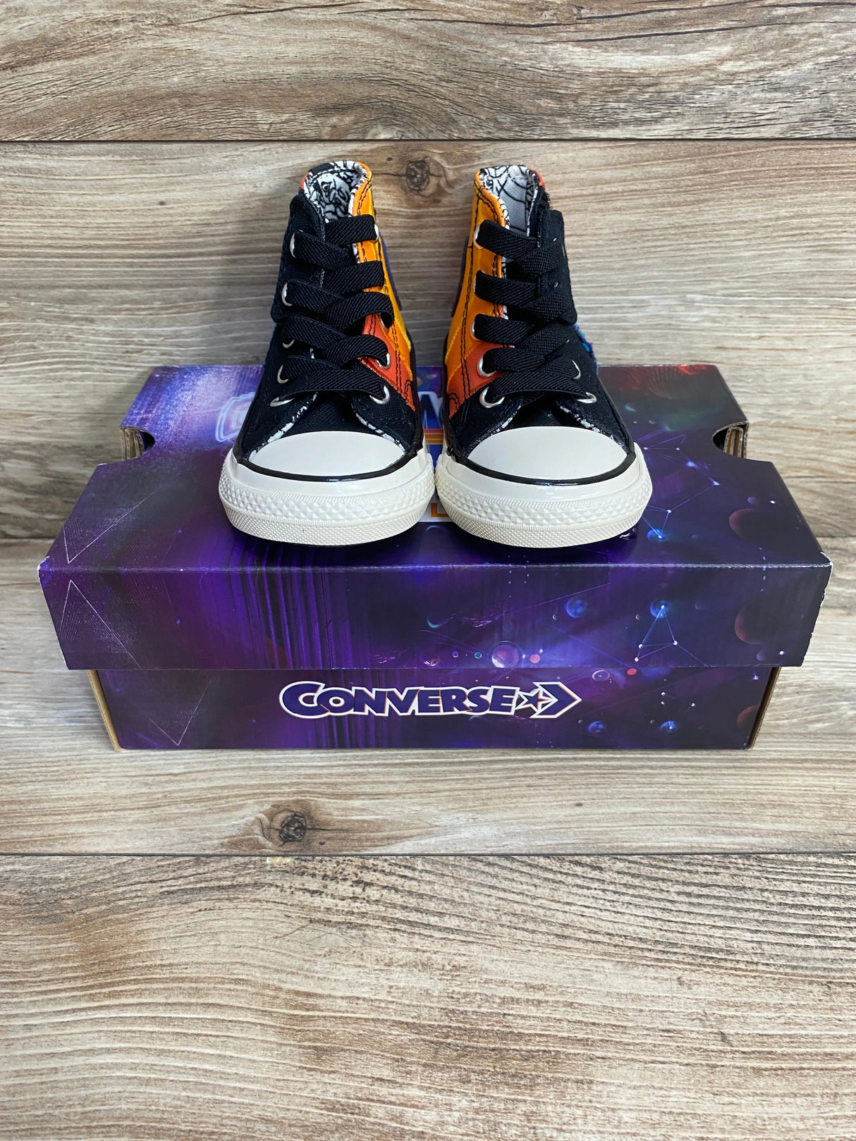 Front view of toddler Converse high-top sneakers with Space Jam Tune Squad orange-black panels on purple box