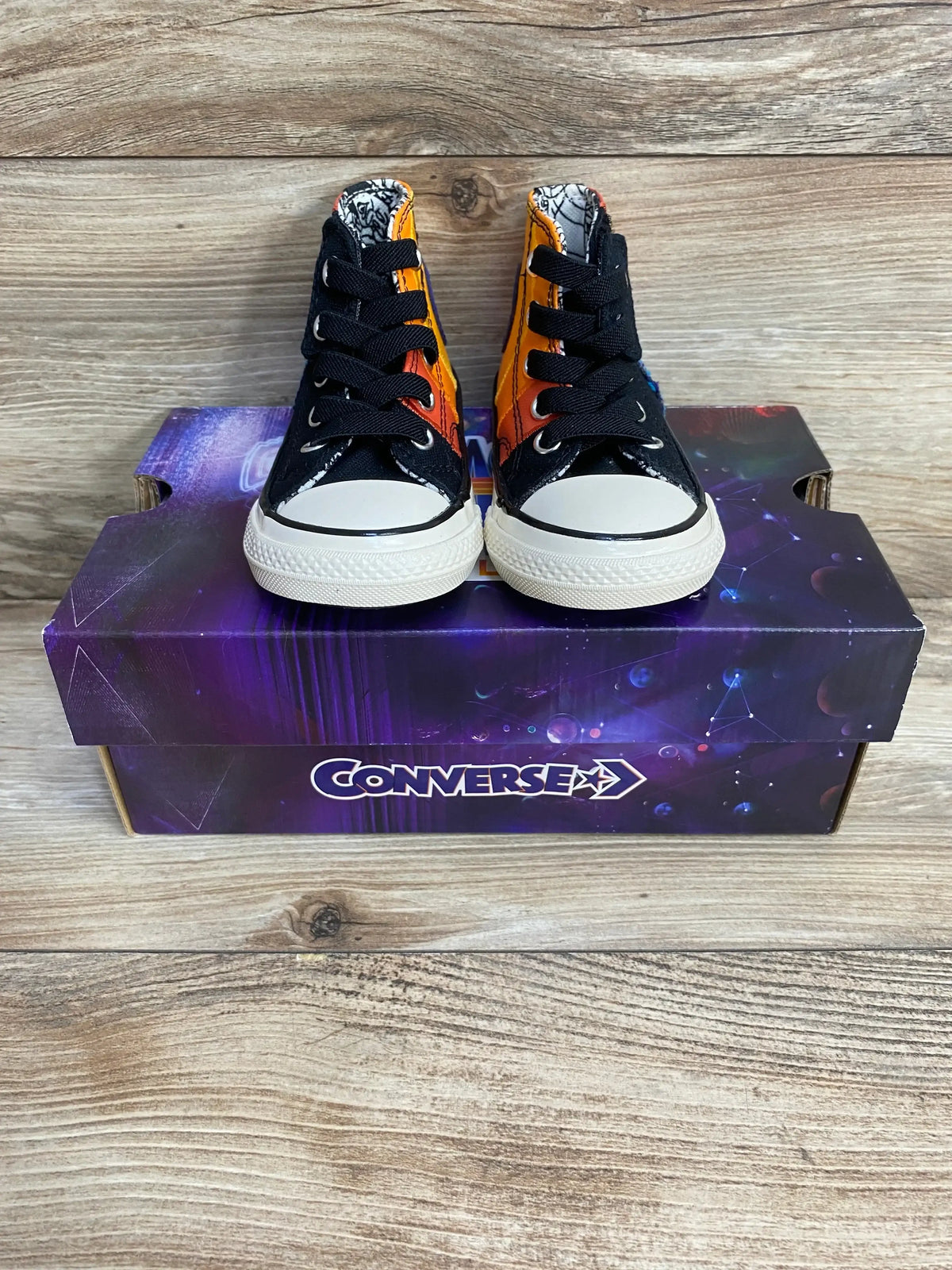 Front view of toddler Converse high-top sneakers with Space Jam Tune Squad orange-black panels on purple box