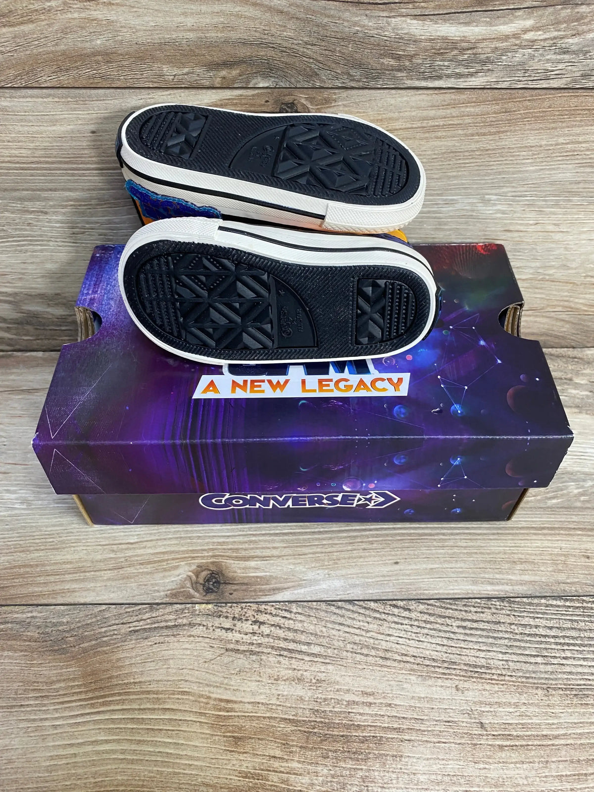 Bottom view of Converse Chuck Taylor All Star Space Jam Tune Squad sneakers on Converse A New Legacy purple box on wood plank floor