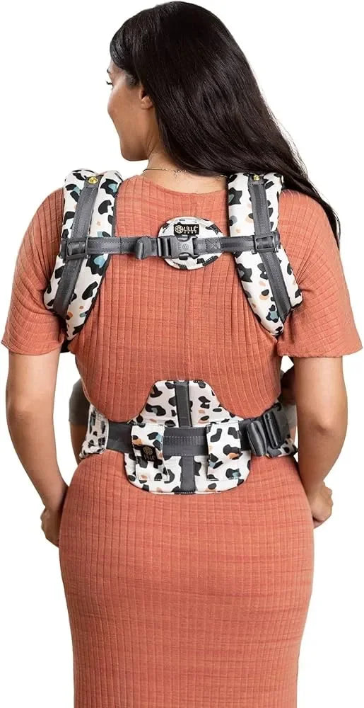 Woman wearing a multi-color spotted baby carrier on back over rust ribbed dress, white background