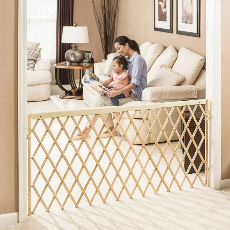 Expandable wooden baby safety gate in doorway, woman and child reading on sofa in background