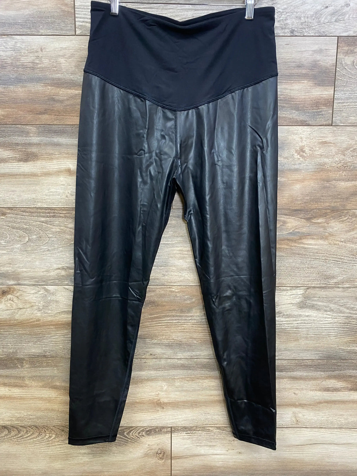 Front view of black Gap maternity vegan leather leggings size XL with high V-shaped stretch waistband on wood background