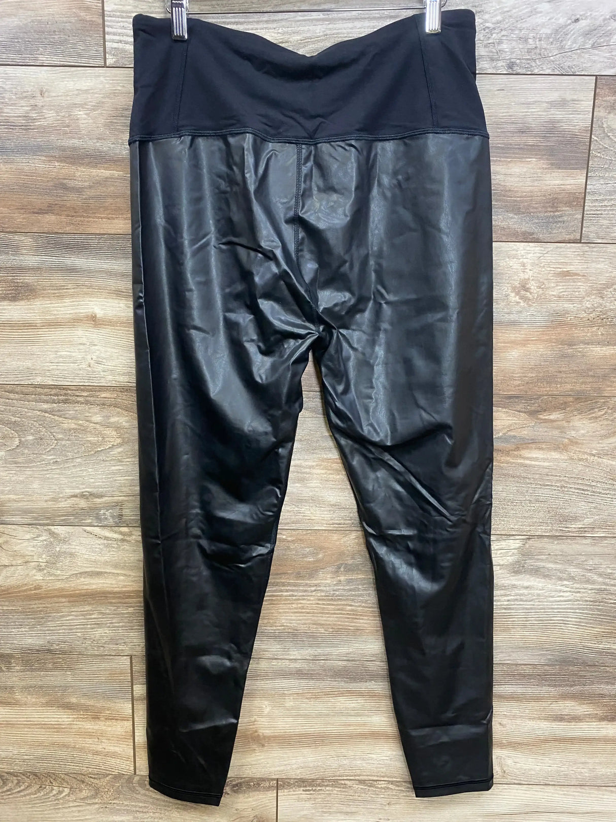 Flat front view of black maternity vegan leather leggings with fold over waistband and shiny finish on wood background