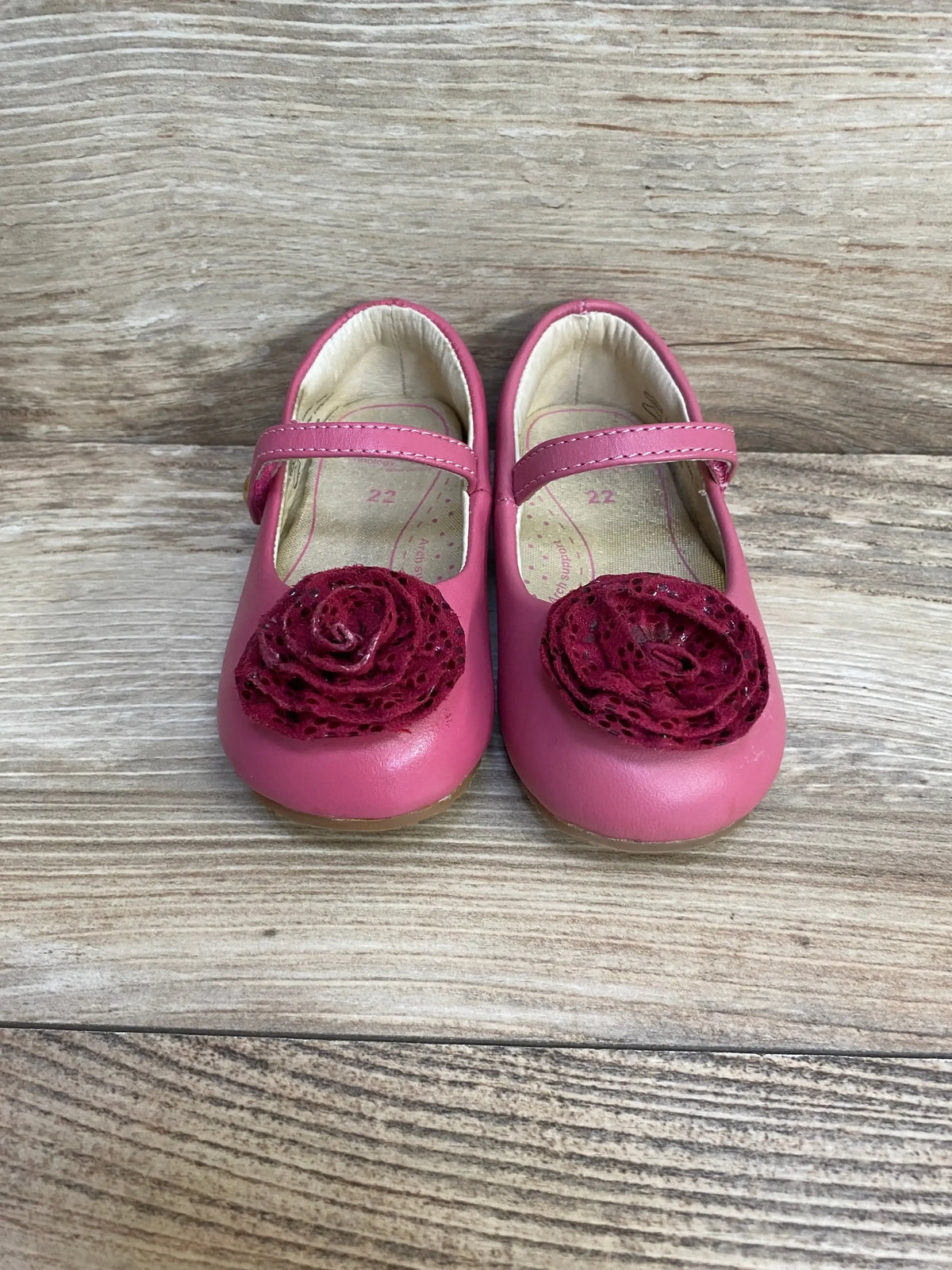 Front view of pink Pediped Mary Jane shoes showing lace flower embellishments with wood background, size 6-6.5C