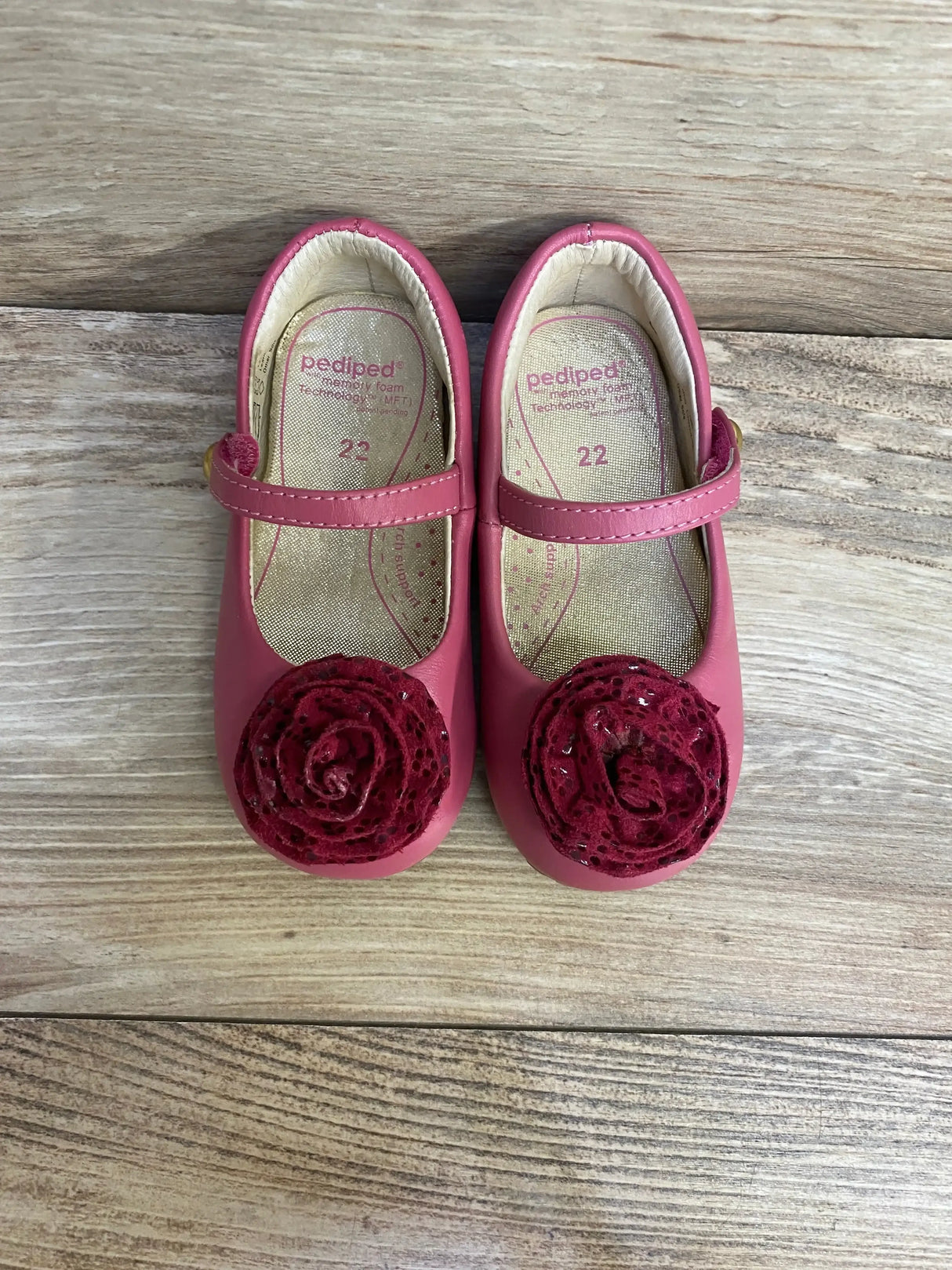 Top view of Pediped Mary Jane toddler shoes with pink leather strap, burgundy rosettes, insole marked 22 on light wood