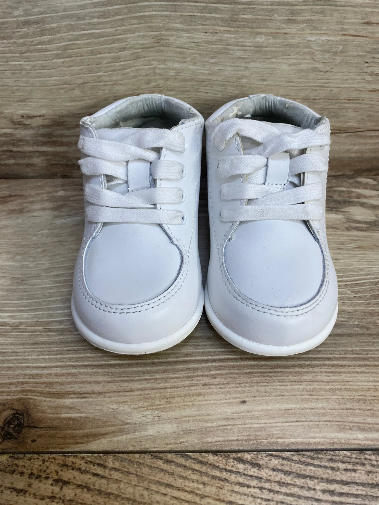 Front view of Smart Step white toddler walking shoes showcasing lace-up design and light wear on the collars on a wood floor