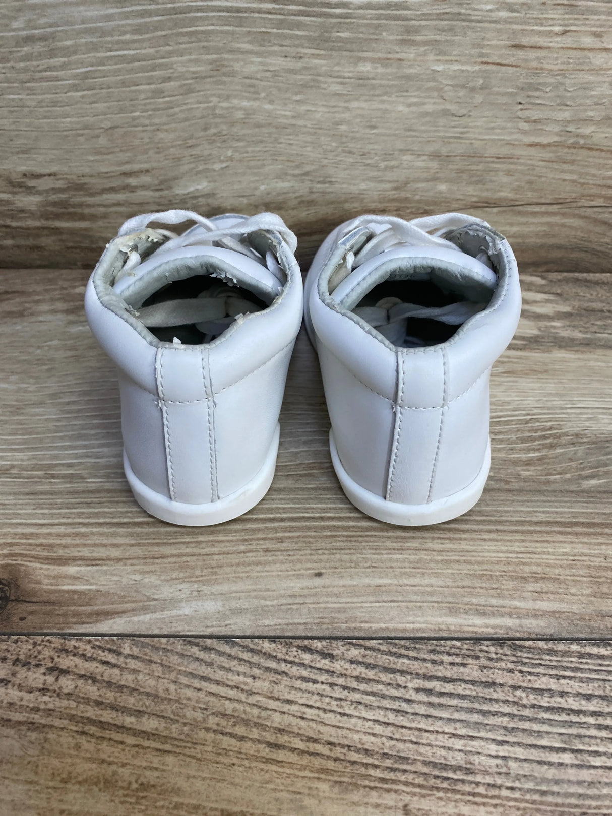 Rear view of white toddler high-top walking shoes size 5C showing worn inner lining and scuffed collars on wood floor