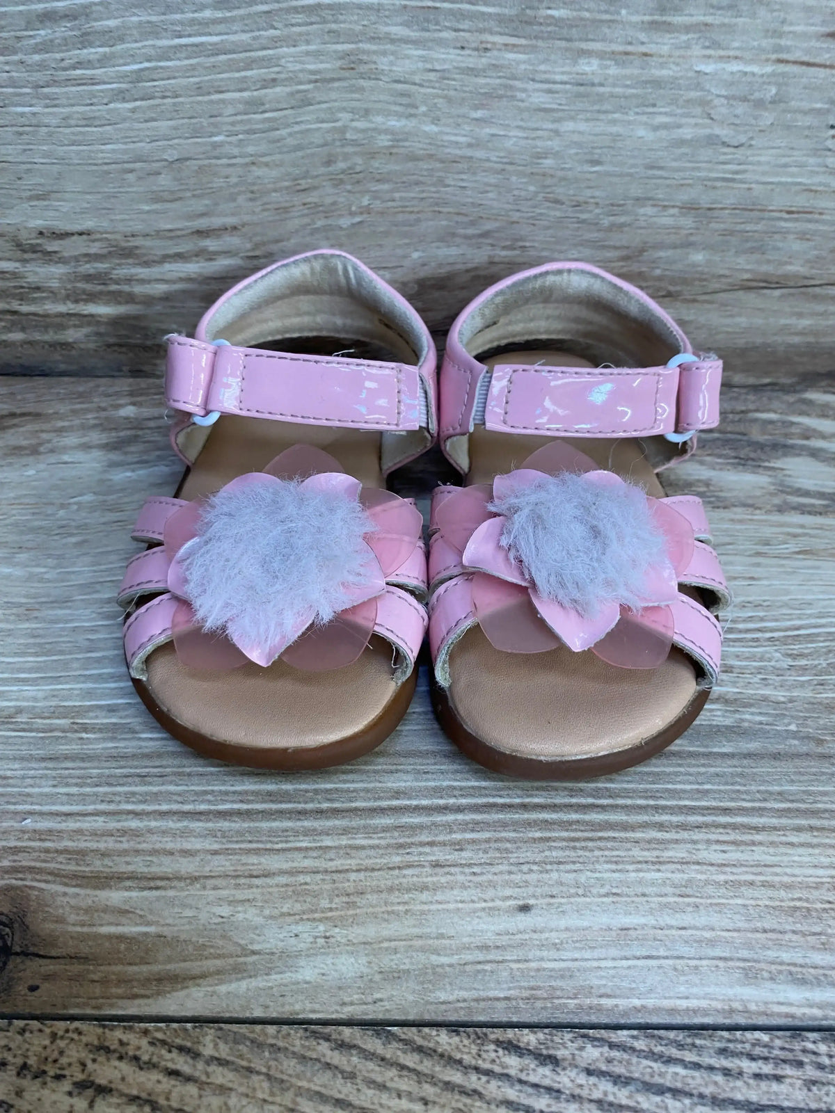 Front view of pink UGG toddler sandals showcasing layered flower embellishments with fuzzy centers on wood background