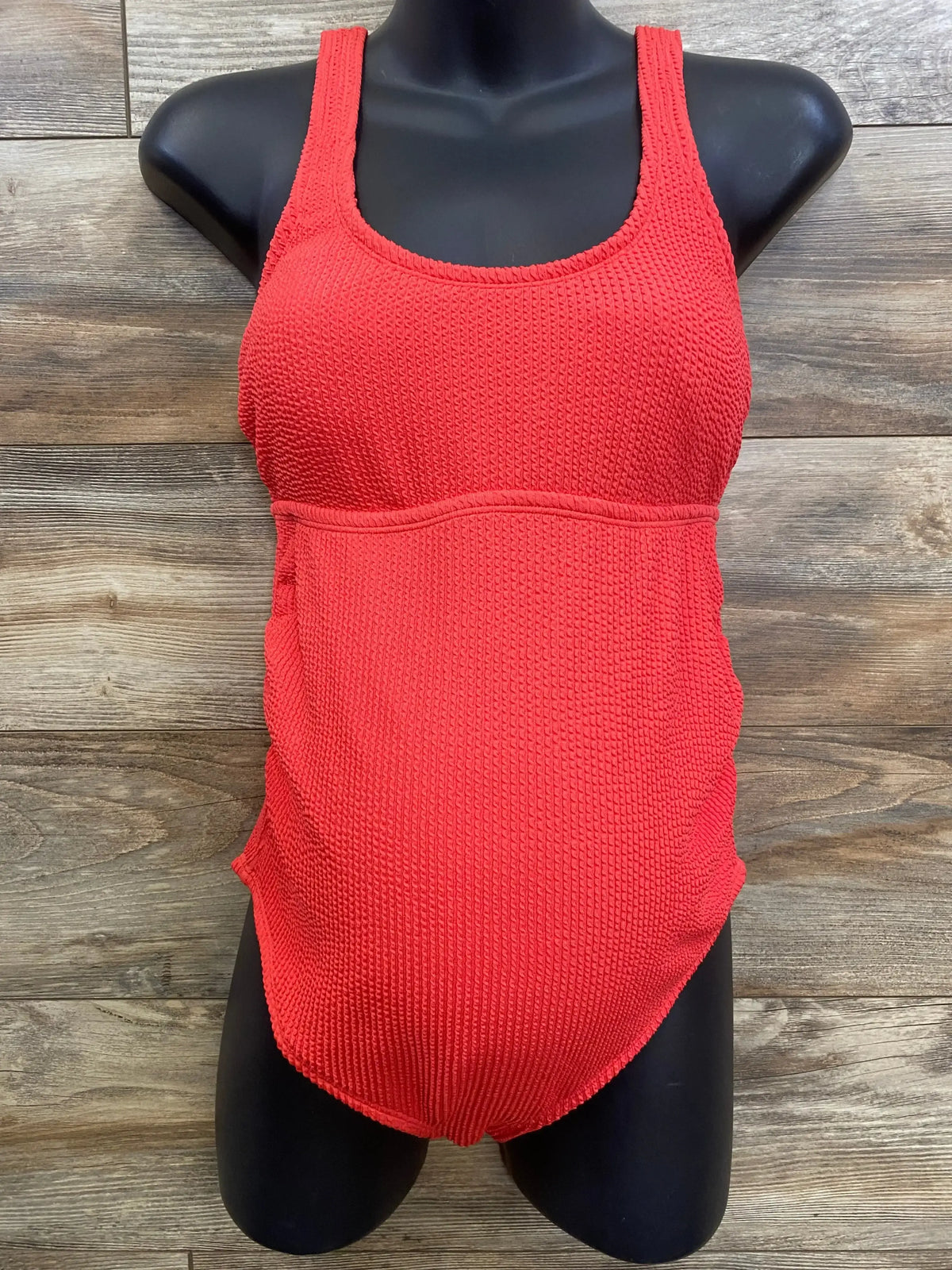 Front of red Isabel maternity one-piece swimsuit XL, textured knit and scoop neck on black mannequin with wood background