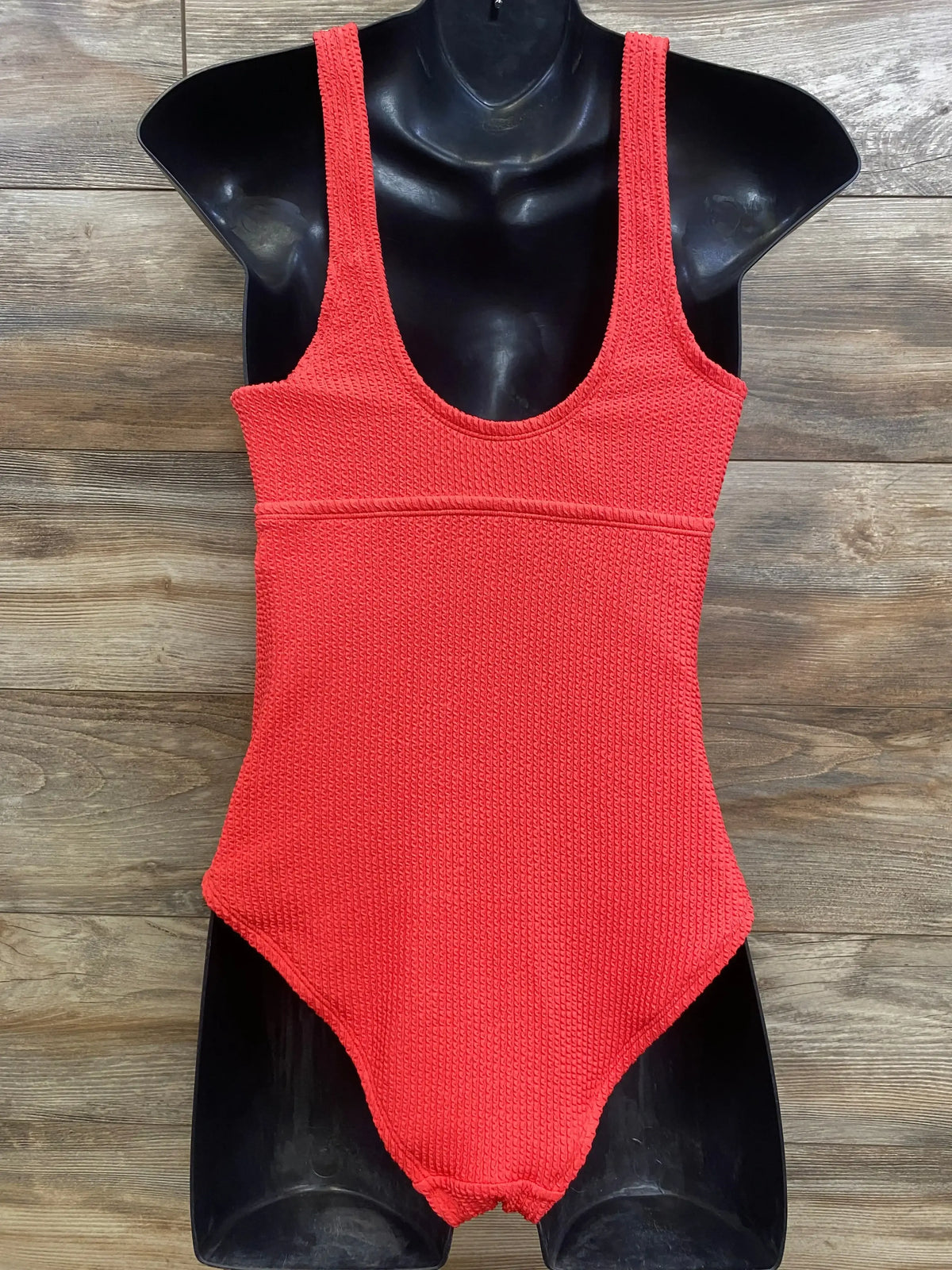 Front view of red Isabel maternity one-piece swimsuit showing textured knit fabric and scoop neckline on black mannequin with wood plank background