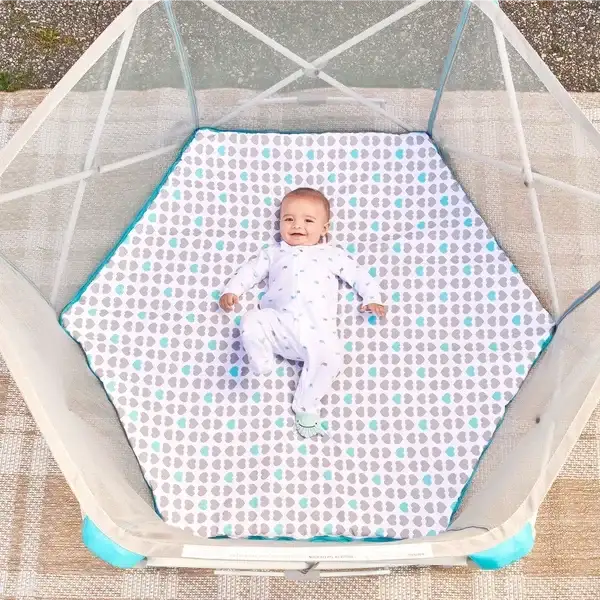 Baby lying on a patterned padded floor inside a Regalo six-panel portable play yard with mesh sides