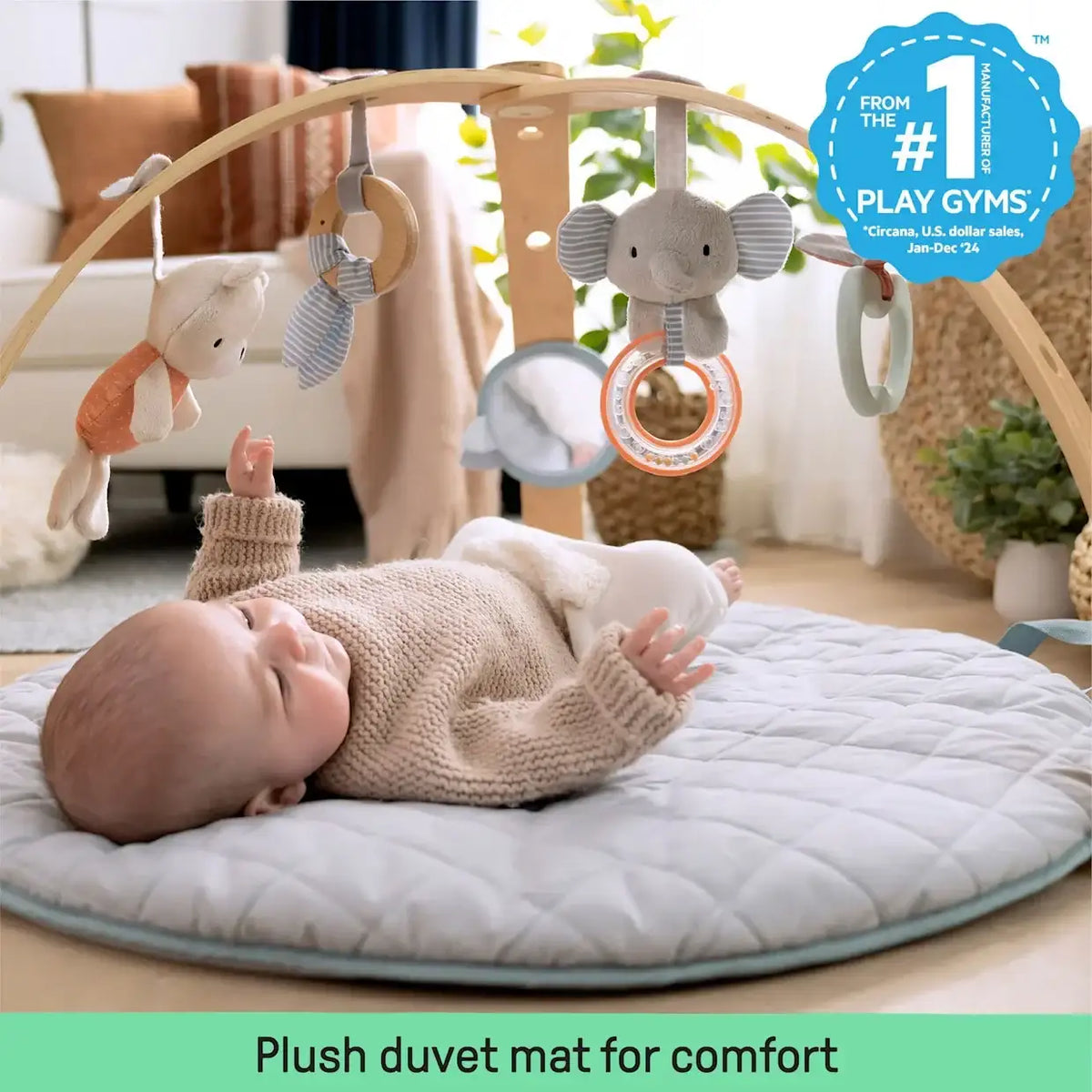 Baby lies on the Ingenuity Cozy Spot play mat beneath a wooden toy bar with hanging toys; plush duvet mat for comfort
