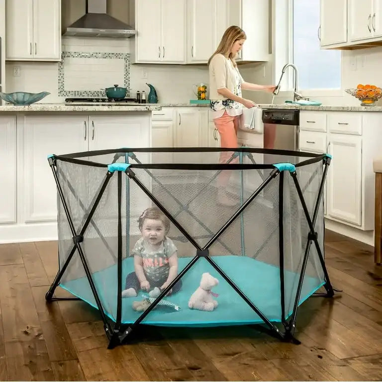 Regalo My Play 6-panel teal portable play yard with mesh sides and teal floor, X-frame supports in a kitchen with toddler