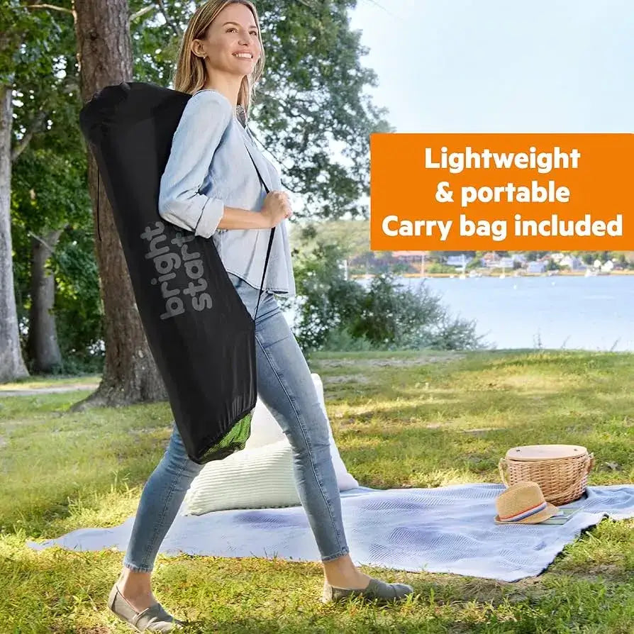 Woman carries a green Bright Starts playard outdoors; lightweight and portable, carry bag included