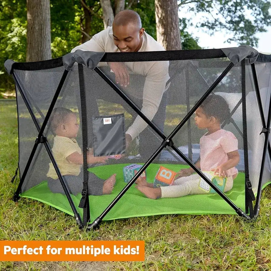 Front view of Bright Starts Pop ‘N Play playard showcasing mesh sides and green floor with two children outdoors
