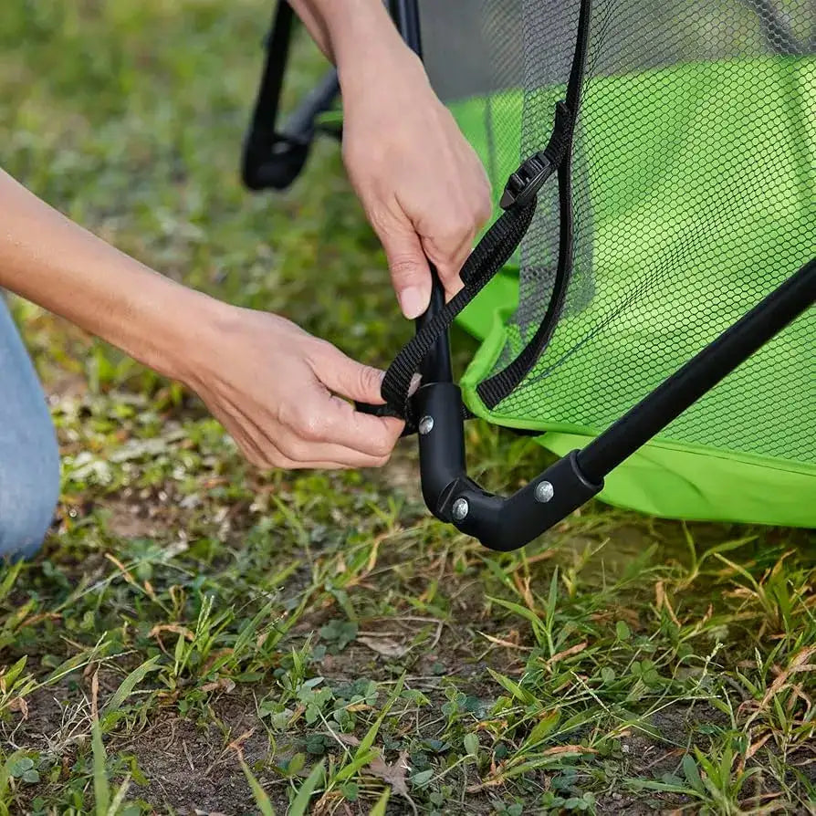 Close-up of green Bright Starts Pop ‘N Play Indoor/Outdoor Playard showing its black strap and buckle on grass