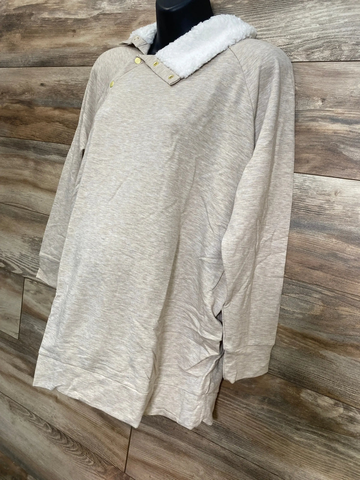 Three-quarter view of oatmeal Isabel maternity sweatshirt showing sherpa snap collar and side ruching on wood panel background
