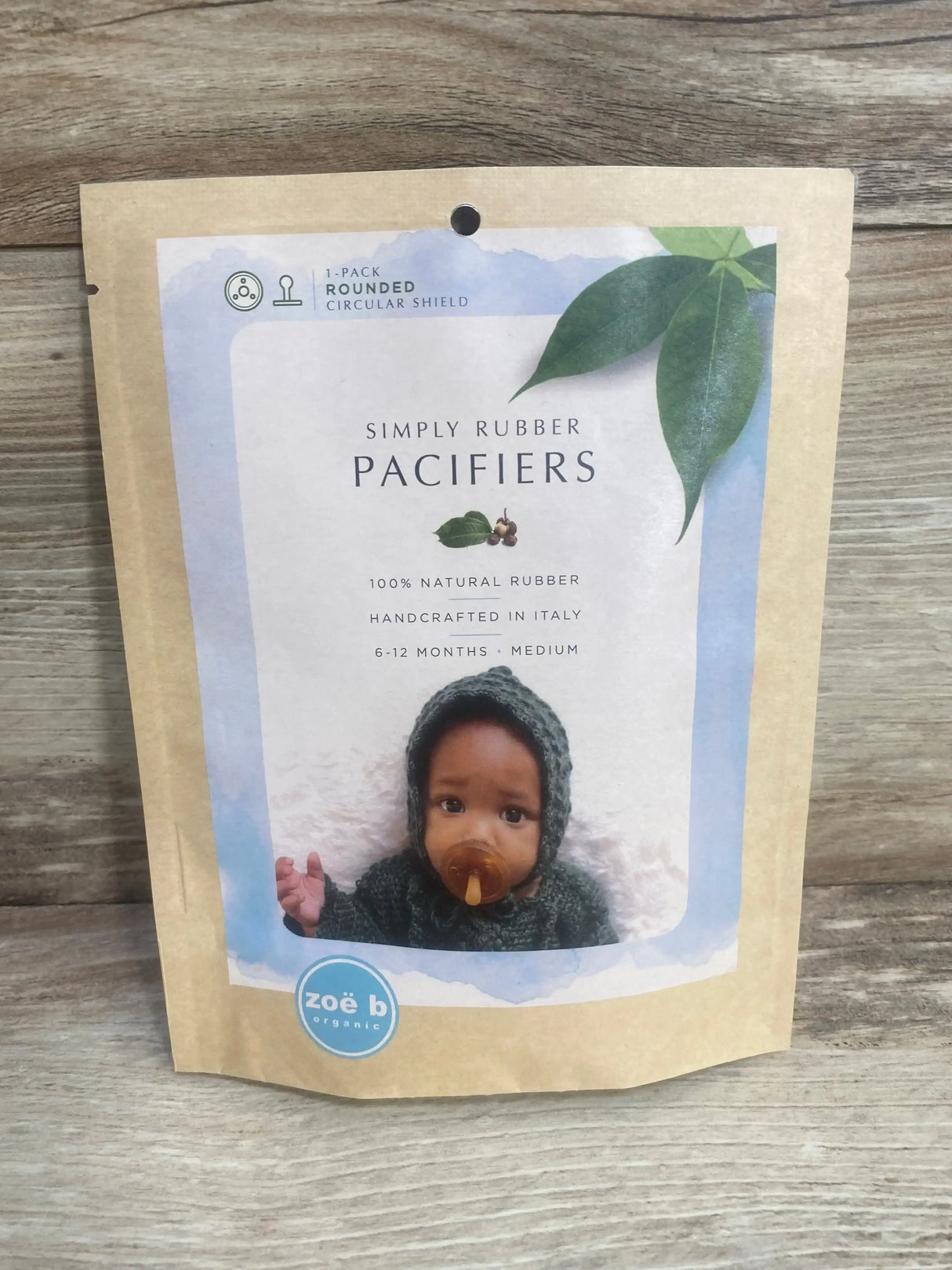 Front of Zoe b Simply Rubber pacifier package showing baby with amber pacifier and Simply Rubber Pacifiers label on wood